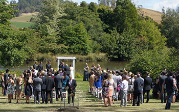 A large number of guests enjoying a wedding ceremony in the sunshine by the edge of Founders Lake at The Tasmanian Arboretum