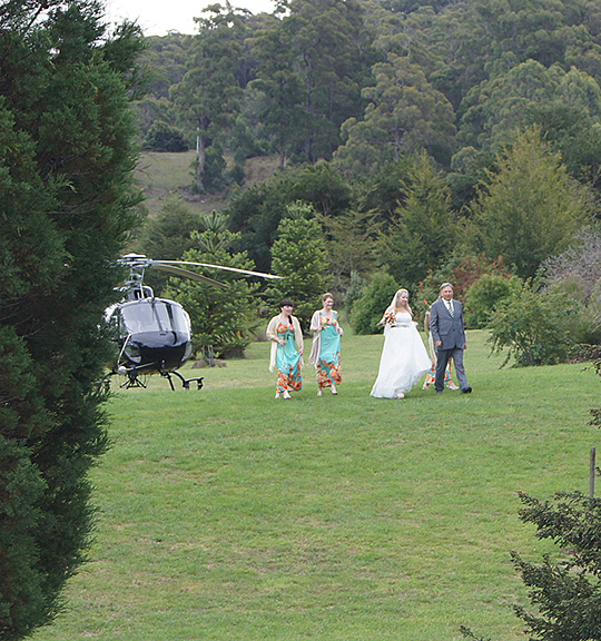 The bride in a long white dress walking across the lawn to her wedding after arriving by helicopter