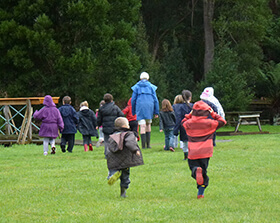 A volunteer educator leads a group of enthusiastic school children towards a bridge over Mellrose Creek at The Tasmanian Arboretum